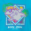 Cartoon shark with sunglasses and a red headband, smiling against a tropical backdrop with palm trees and sun. Text below reads Ron Jon Surf Shop.