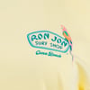 Close-up of a yellow shirt featuring the Ron Jon Surf Shop Cocoa Beach logo with a colorful parrot graphic.