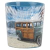 A ceramic mug featuring an illustration of a vintage woodie car on a sandy beach with ocean waves and sun rays in the background.