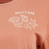 A close-up of a rust-colored shirt featuring white graphic designs of seashells and a starfish with the text RHYTHM Ron Jon Surf Shop.