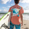 Man holding a surfboard on a beach, wearing an orange T-shirt with a wave design and text Ron Jon Surf Shop. Ocean and clouds in the background.