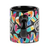 A black ceramic mug with a colorful geometric pattern and bold letters, featuring a black handle and the Ron Jon Surf Shop logo printed on it.