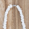 A close-up of a white shell necklace with a silver clasp, laid in a partial circle on a wooden surface.