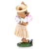 Side view of a small pig figurine wearing sunglasses, a straw hat, a hula skirt, and a floral lei, standing on a decorative base against a white background.