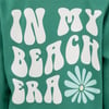 Green sweatshirt with white text IN MY BEACH ERA and a blue and white flower below the text.