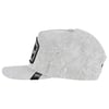 A light grey, textured flat-brim cap viewed from the side, featuring a black rectangular patch with white text on the front.