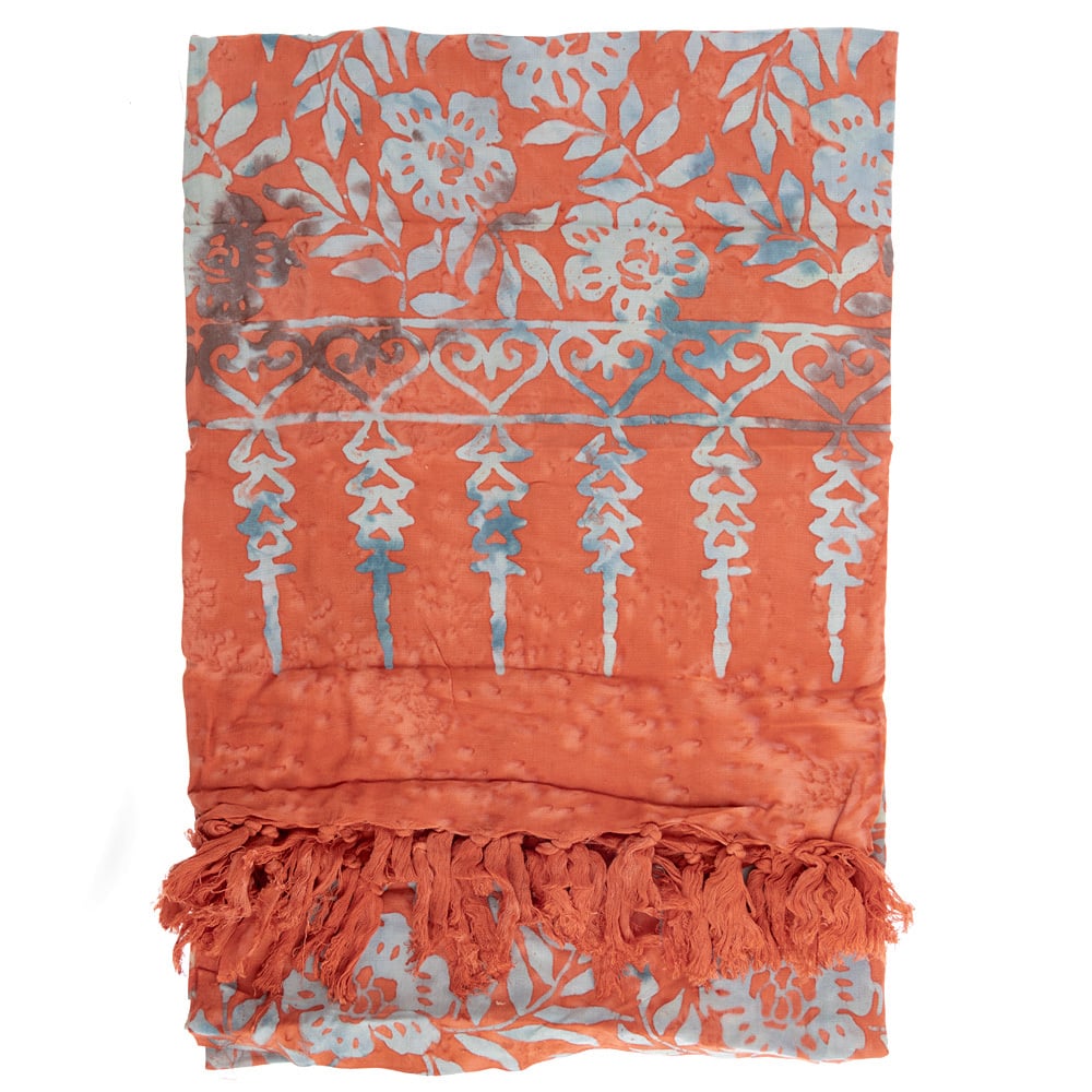 A folded orange sarong with blue floral and geometric patterns and a fringe border at one end.