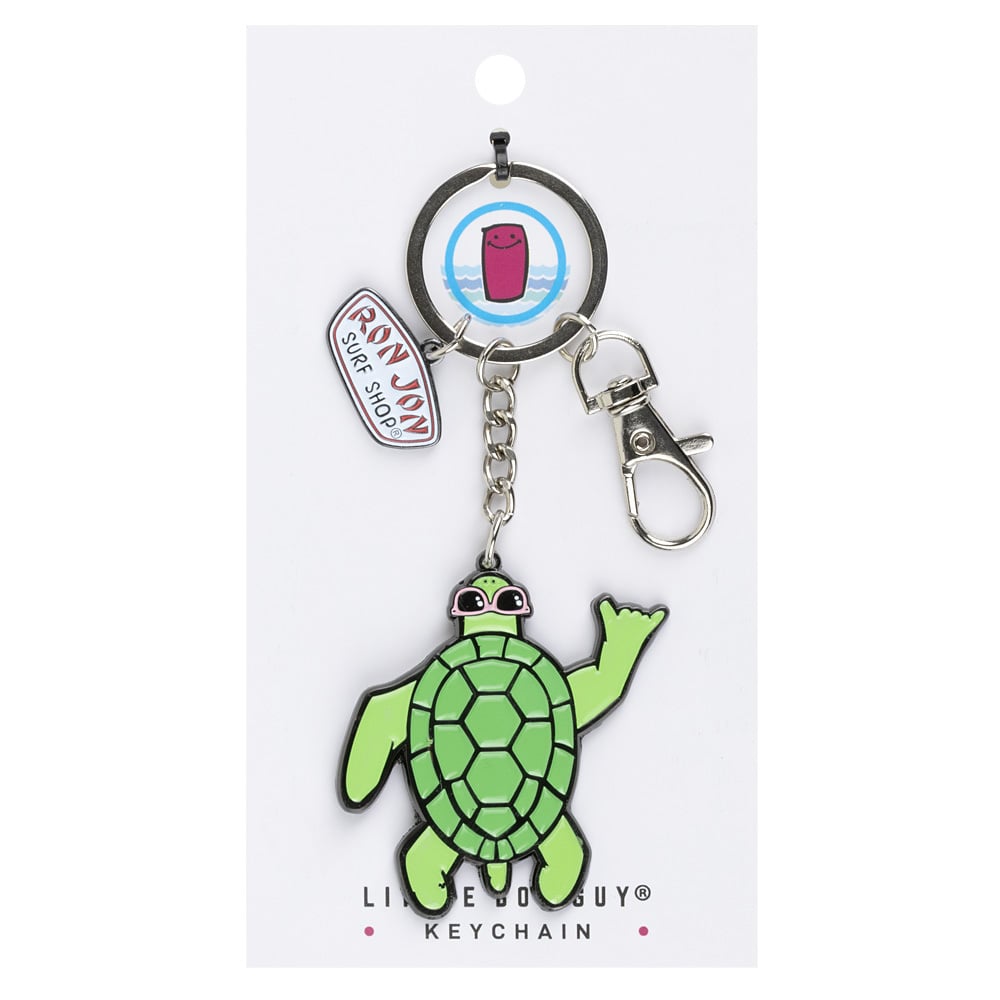 A keychain featuring a green cartoon turtle, a Ron Jon Surf Shop charm, and a round charm, attached to a metal keyring and clasp.
