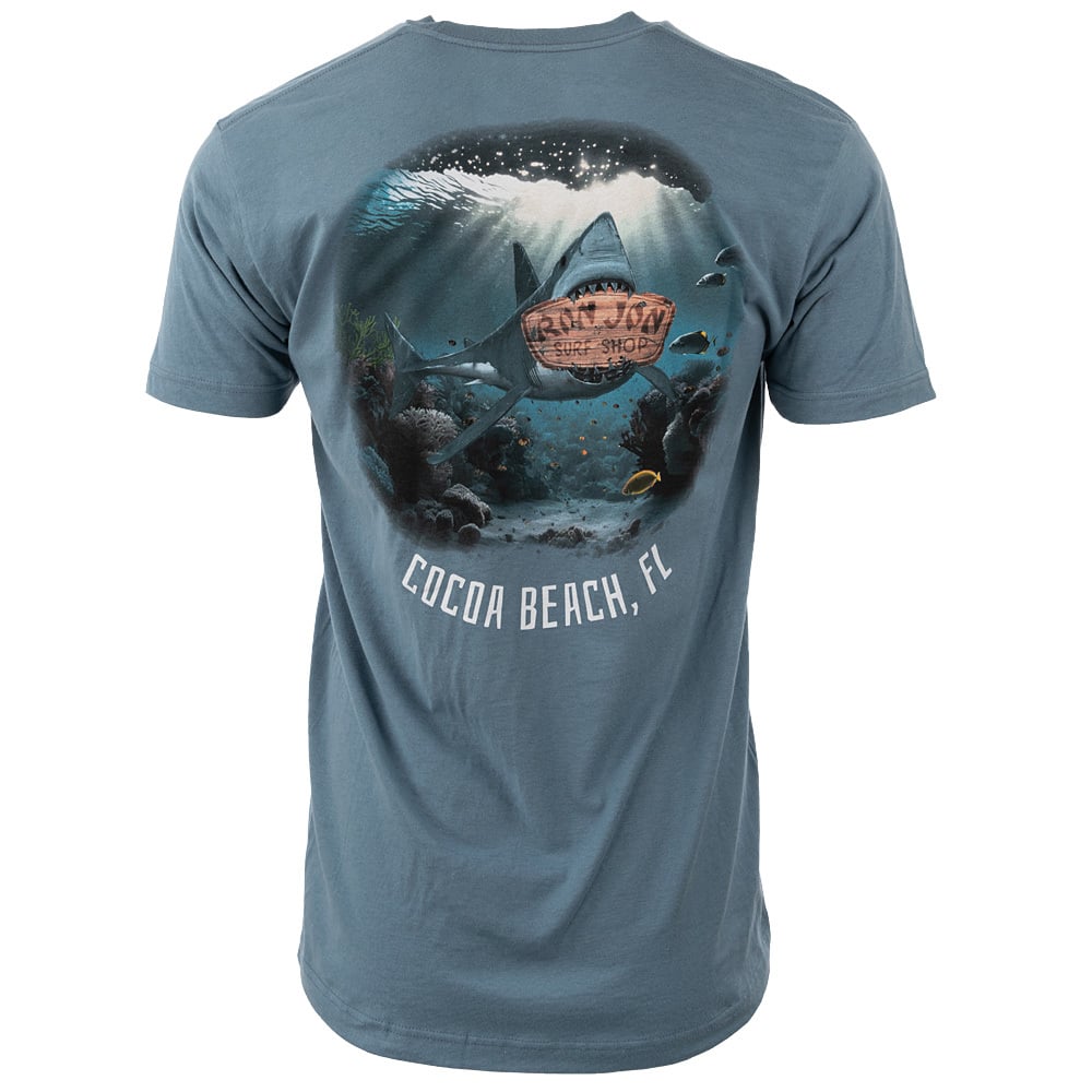 Blue T-shirt featuring an underwater scene with a shark and a rusty barrel, with text Cocoa Beach, FL. The back of the shirt displays the design.