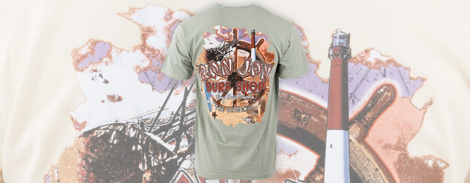 A light green t-shirt featuring a colorful graphic with the words Ron Jon Surf Shop on the back, set against a background with a lighthouse illustration.