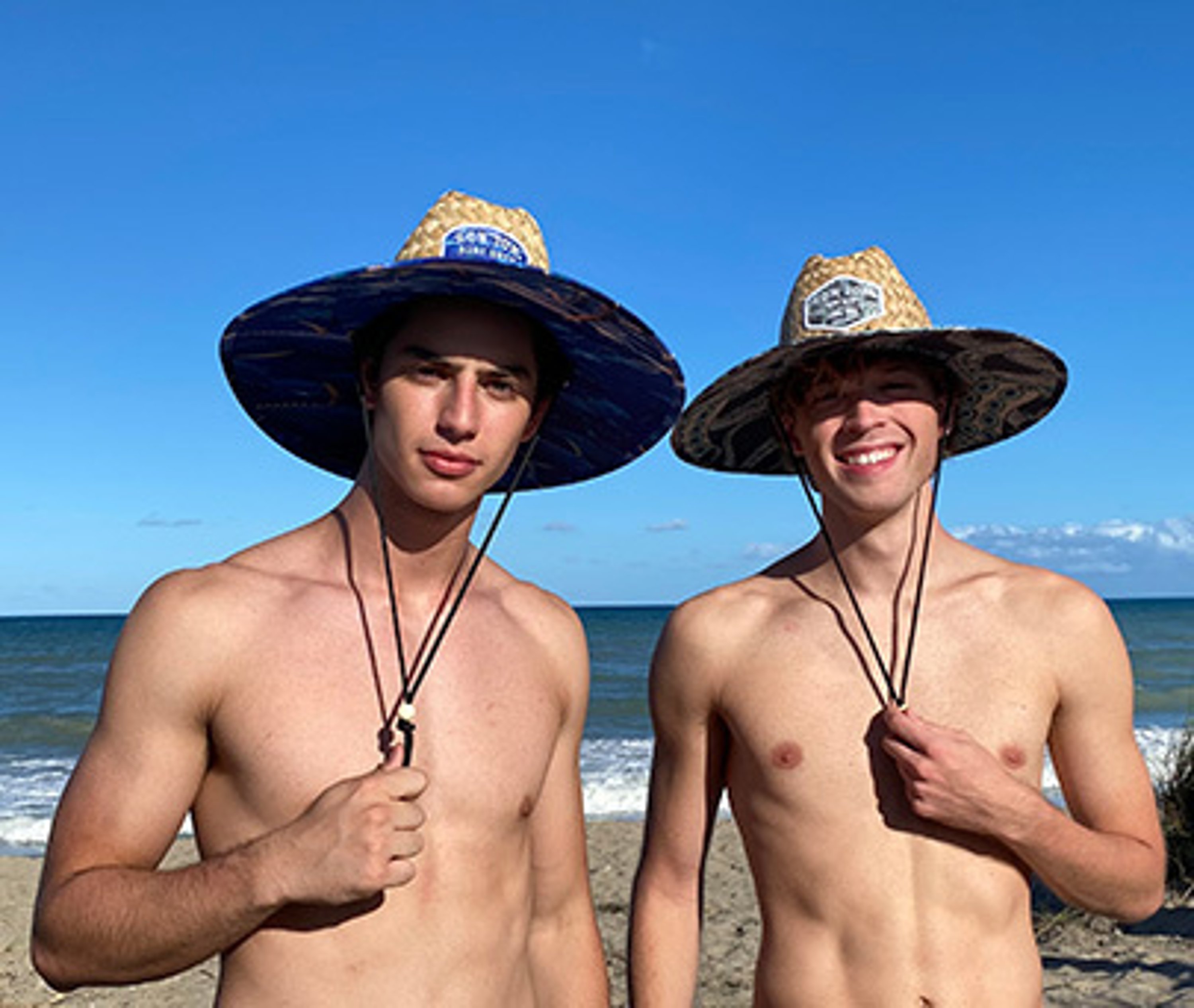 two guys standing on the beach wearing straw lifeguard hats