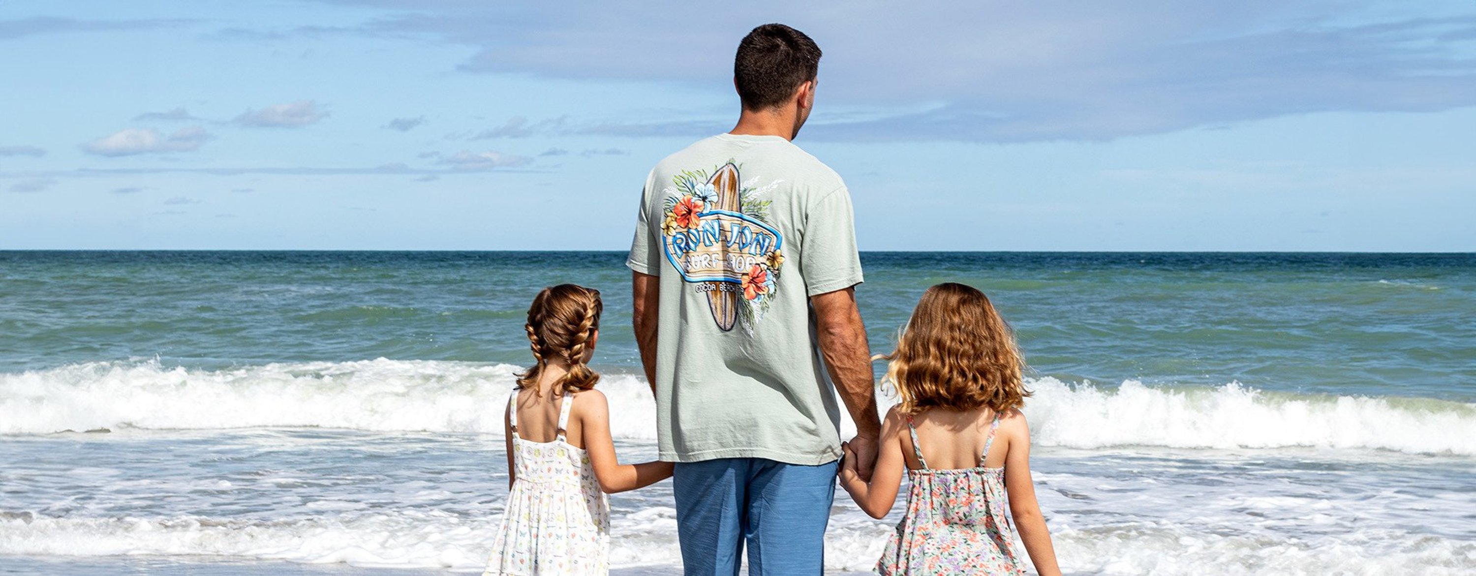 a dad standing at the edge of the ocean with two young daughters looking out to sea