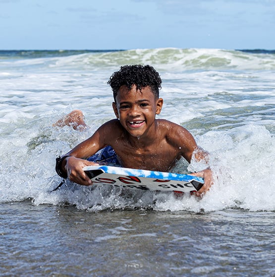A young boy smiling while riding a small wave on a bodyboard at the beach.