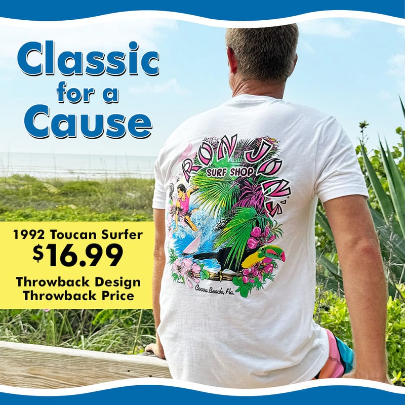 Guy sitting on boardwalk at beach wearing Ron Jon Toucan Tee